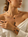 Woman wearing a Black necklace and bracelet with black stones, holding her hand to her chest.