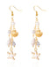 Boucles d'oreilles en or et perles ornées d'étoiles de mer et de coquillages sur fond blanc