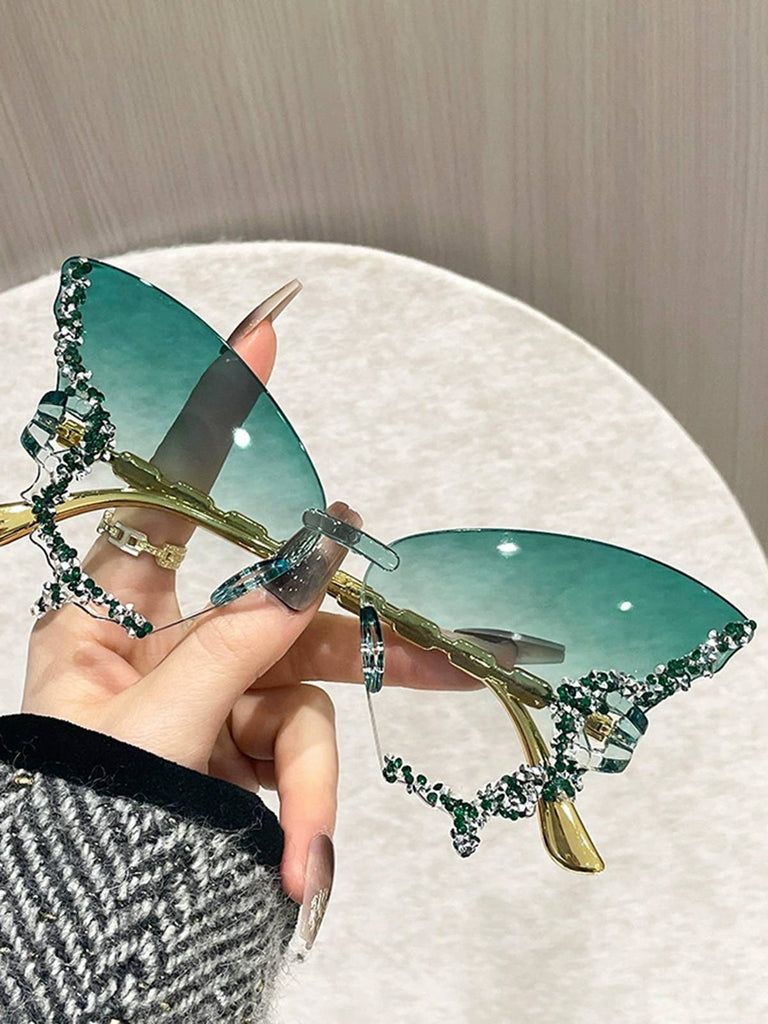 Sunglasses with decorative gold and green frame held by a hand against a neutral background