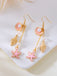 Paire de boucles d'oreilles ornées de coquillages, d'étoiles de mer et de perles sur fond blanc.