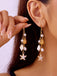 Gold earrings with starfish and shell designs being worn by a person.
